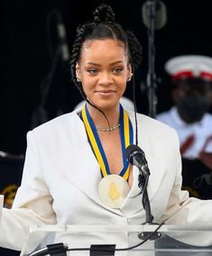 a woman standing at a podium with a medal around her neck and wearing a white suit