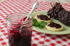 grapes and jam are on a plate next to crackers, with a spoon in the jar