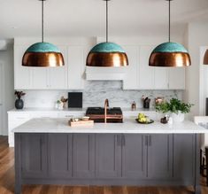 a kitchen with three pendant lights hanging from the ceiling and marble counter tops on the island