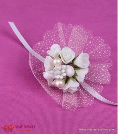 white flowers and pearls are on a pink cloth with a ribbon in the shape of a flower