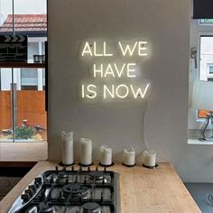 a neon sign that says all we have is now on the wall above a stove