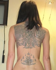 a woman with tattoos on her back standing in front of a wall