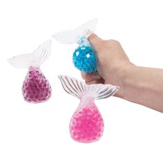 a hand is holding two small plastic mermaid tail ornaments, one pink and the other blue