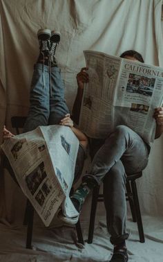 two people sitting in chairs reading newspapers