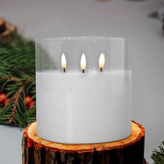 three lit candles sitting on top of a tree stump