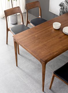 a wooden table with two black chairs and a white plate on it in front of a window