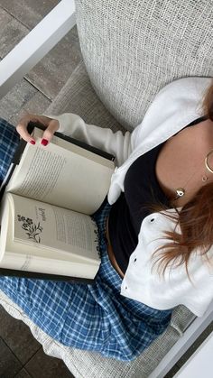 a woman sitting on a chair holding an open book in her lap and looking at the camera