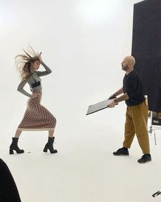 a man and woman are walking in front of a photo studio with one holding a large piece of paper