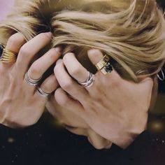 a woman covering her face with her hands and wearing rings on her fingers, looking down at the ground