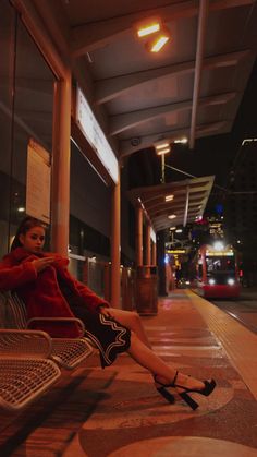 a woman sitting on top of a metal bench next to a bus stop at night