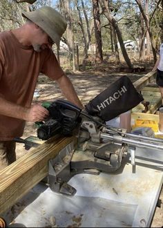 two men are working on a piece of wood in the woods while another man watches