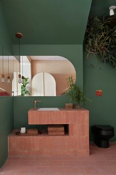 a bathroom with green walls and tiled flooring next to a plant on the wall