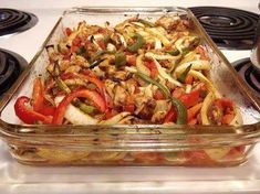 a glass casserole dish filled with chicken, peppers and onions on the stove