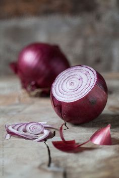 two red onions sitting on top of a wooden table next to one onion slice and another sliced in half