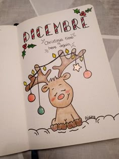 an open notebook with a drawing of a reindeer and christmas lights hanging from it's antlers