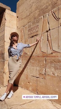 a woman standing in front of an ancient wall with egyptian art on it's side