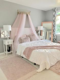 a pink canopy bed in a bedroom next to a mirror and dresser with two lamps