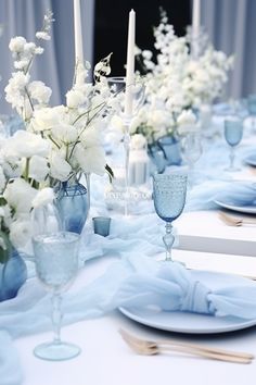 the table is set with white flowers and blue napkins, silverware and candles