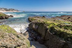 the beach is covered in green mossy rocks and blue water with houses in the distance