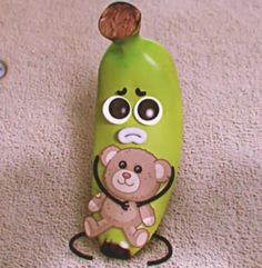 a green banana with a brown teddy bear on it's head sitting on the floor