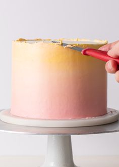 a person using a knife to cut a cake with pink and yellow frosting on it