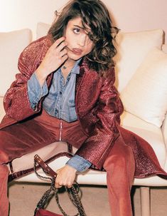 a woman sitting on top of a couch holding a handbag in her right hand