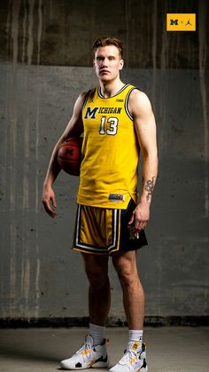 a man in a yellow uniform holding a basketball and posing for the camera with his hands on his hips