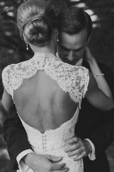 a bride and groom embracing each other in black and white, with their back to the camera