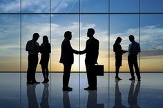 silhouettes of business people shaking hands in front of large windows