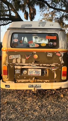 an old van with stickers on it parked in the dirt next to some trees