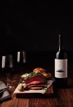 a bottle of wine sitting next to a sandwich on top of a wooden cutting board