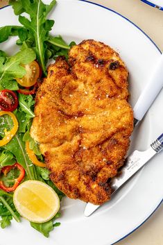 a white plate topped with fried chicken next to a green salad and lemon wedges