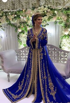 a woman in a blue and gold gown standing next to a white couch with flowers on it