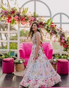 a woman standing in front of a pink couch wearing a floral dress and holding a flower crown