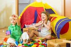 two children playing with toys on the floor in front of a tent and play table