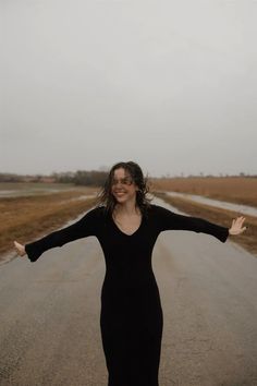 a woman standing in the middle of an empty road with her arms spread wide open