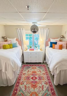 two twin beds with colorful pillows in a room next to a rug on the floor