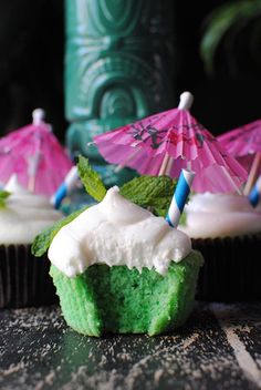 green cupcakes with white frosting and pink parasols on the top