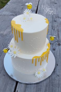 a three tiered cake with daisies and bees on the top is sitting on a wooden table