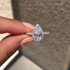 a woman's hand holding an engagement ring with a pear shaped diamond on it