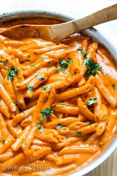 a large pot filled with pasta and parsley on top of a wooden table next to a spoon