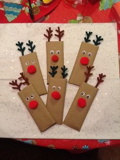 three reindeer made out of brown paper bags on top of a white tablecloth with red noses and nose decorations