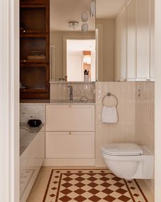 a white toilet sitting next to a sink in a bathroom under a mirror on top of a tiled floor