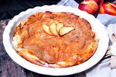 an apple pie is in a white dish on a wooden table next to some apples