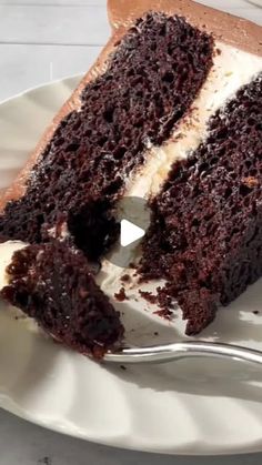 a piece of chocolate cake with white frosting on a plate and a fork next to it