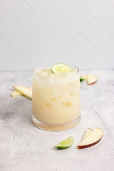 an apple margarita sits on a marble counter top with sliced apples and limes around it