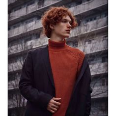 a young man with red hair wearing an orange turtle neck sweater and black blazer