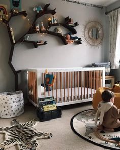 a baby sitting in a crib next to a tree with lights on the branches