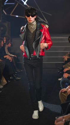 a man walking down a runway wearing a red leather jacket