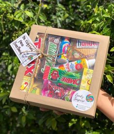 a person holding up a box with various items in it on top of some bushes